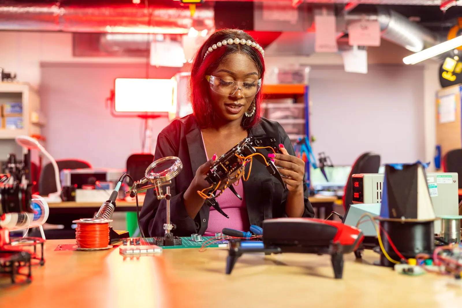 Black female engineer at desk assembling drones, showcasing electronics and technology in a modern lab setting.